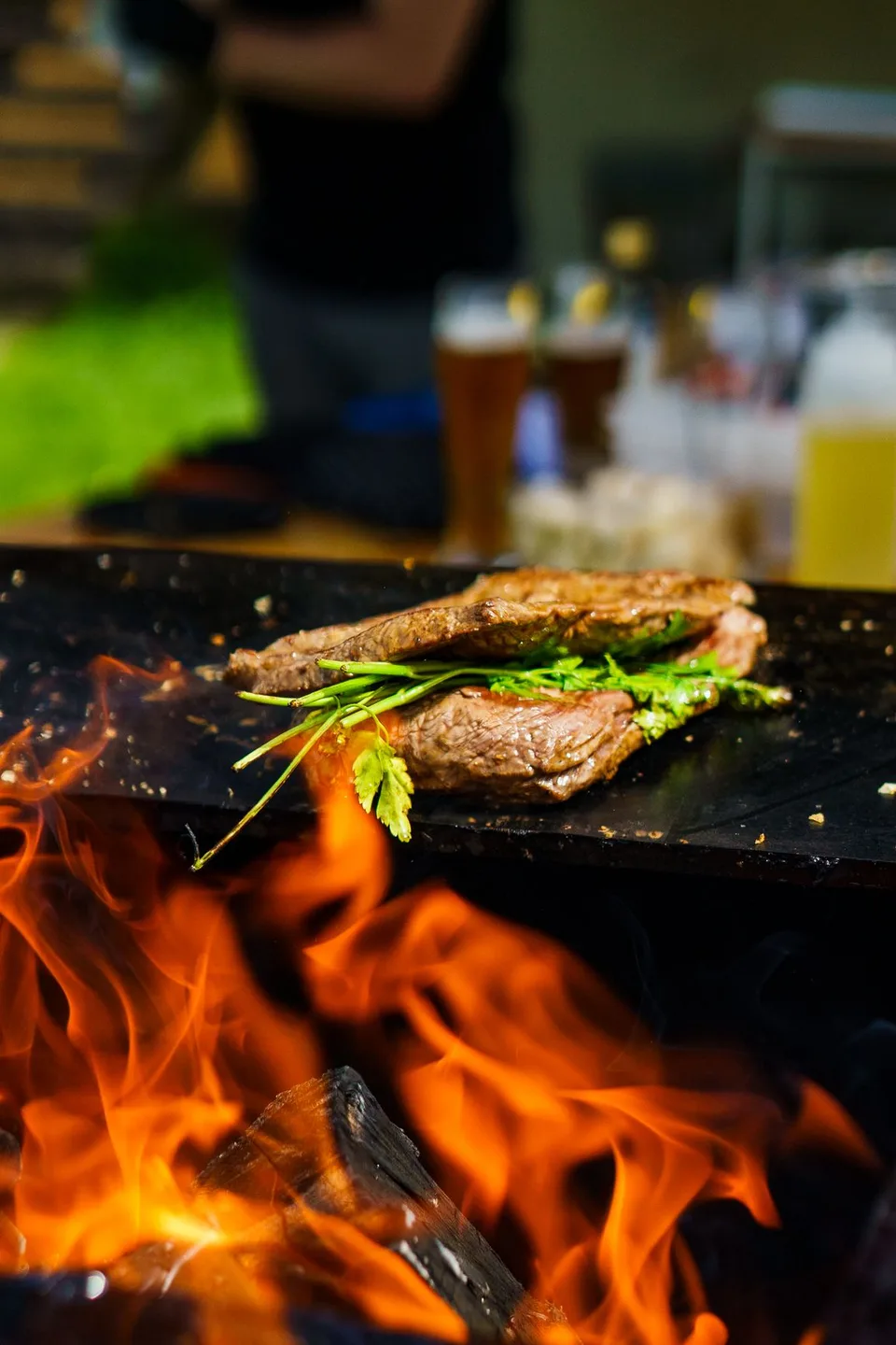 Flammen unter der Grillplatte, darüber Fleisch und frische Kräuter