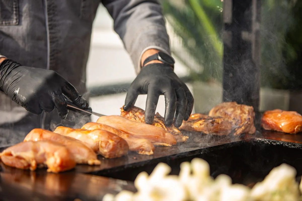 Hände bei der Zubereitung auf einer heißen Grillplatte, von der Dampf aufsteigt